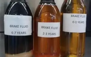 three jars. One shows black brake fluid, 6-7 years old. One shows red, brown brake fluid, 2-3 years old. Once shows yellow brake fluid, 0-1 years old